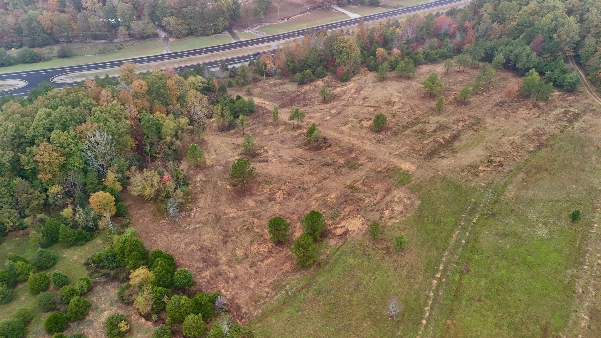 Aerial view of cleared land with trees and foliage, near a highway surrounded by colorful autumn leaves.